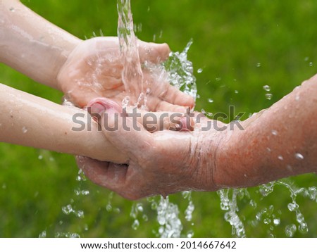 The concept of heritage and nature conservation on Earth.Water pours into the hands of a child in the hands of an older grandmother against a background of green grass.