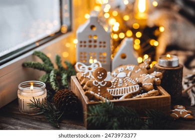 Concept of home christmas or new year celebration, family traditions. Assortment of gingerbread cookies with icing in a vintage wooden box on a window sill with atmospheric lights - Powered by Shutterstock