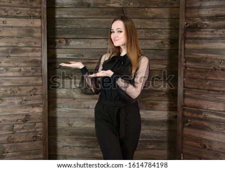 The concept of home comfort. Photo of a pretty brunette girl with excellent make-up in dark clothes standing on a wooden background in the home interior, smiling.