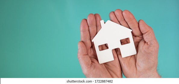 Concept Of Home Insurance With Paper House In Hands On Turquoise Color Background