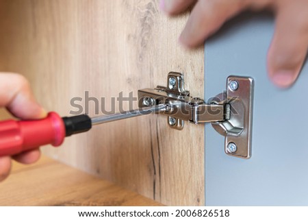 Concept of home repairing. A hand of a furniture assembler adjusting a mechanism for opening the door of the office table with a screwdriver. Close up. Self-assembly of furniture.