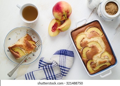 Concept Of Home-baked Food. Diet Yogurt Sponge Cake With Peaches On Table With Tea Pot, Kitchen Cloth And Brown Sugar. Top Down View.