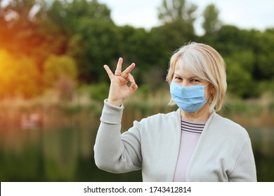 Concept of hope from COVID-19. Mature woman in protective mask with smile shows the OK sign, everything will be fine with hope for the future. A woman over 60 years old with gray hair. - Powered by Shutterstock