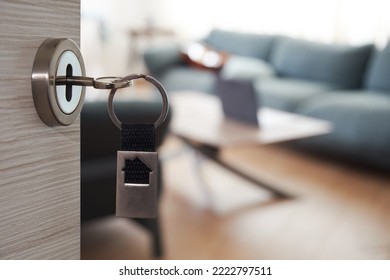 Concept of house selling. Key with house symbol on chain. Opened door and blurred interior