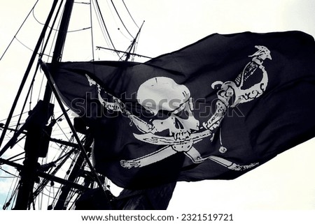 Concept of illegality and piracy: Detail of a real pirate flag with skull and shinbone called Jolly Roger fluttering in the wind among the rigging of an ancient wooden pirate ship