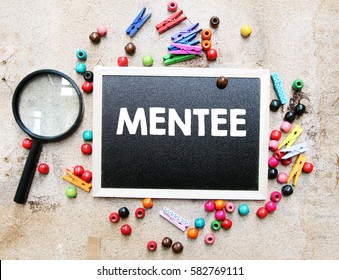 A concept image of a colorful beads and cute clothespin with a magnifying glass over a brown texture background with a chalkboard and a word MENTEE