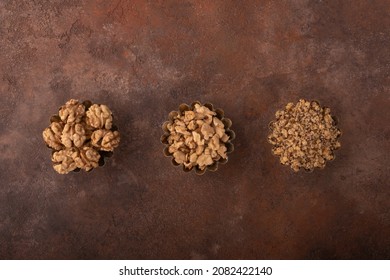 Concept image of different states of the walnut kernel. Whole walnut kernels, walnut pieces, crushed walnuts in vintage iron baking dishes on a harmonious rusty background. ?opy space view.