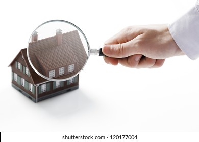 Concept image of a home inspection. A male hand holds a magnifying glass over a miniature house. - Powered by Shutterstock