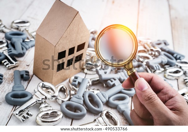 Concept image of a home\
inspection. A male hand holds a magnifying glass over a miniature\
house.
