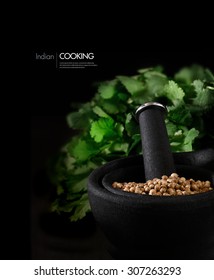 Concept Image For Indian Cooking Ingredients. Coriander Seeds, Also Known As Cilantro, In A Stylish Black Granite Mortar And Pestle With Fresh Coriander Leaves Behind Against Black. Copy Space.