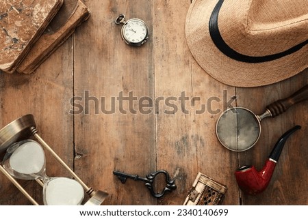 Concept image of investigation or private detective. Fedora hat, magnifying glass and vintage items over wooden table