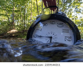 Concept image losing track of time, time running out relativity science image, flowing time, large clock in a flowing stream with half submerged with ripples and colors distorting the numbers.  - Powered by Shutterstock
