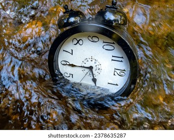 Concept image losing track of time, relativity science image, flowing time, large clock in a flowing stream with half of the clock face submerged with ripples and colors distorting the numbers - Powered by Shutterstock