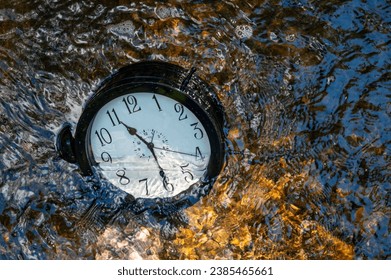 Concept image losing track of time, relativity science image, flowing time, large clock in a flowing stream with half of the clock face submerged with ripples, pebbles and distorted numbers - Powered by Shutterstock