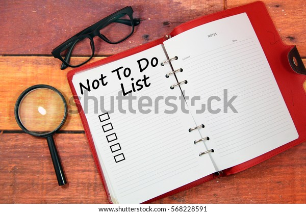 A concept image of an open red diary with spectacles and magnifying glass over a wooden background with a word Not To do List and a Square checkbox 