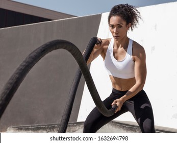 Concept image - Powerful fitness woman training with black battle ropes crossfit at outdoor, with white top - Shutterstock ID 1632694798