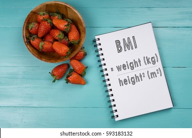 Concept image, strawberry with notebook on a blue wooden background with words Body Mass Index. Health concept.