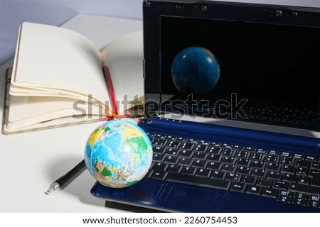 concept image for using digital worl all around the world by showing a laptop with a close up of a world globe, pencil and a paper notebook in the background