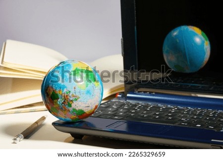 concept image for using digital worl all around the world by showing a laptop with a close up of a world globe, pencil and a paper notebook in the background