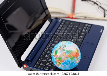 concept image for using digital worl all around the world by showing a laptop with a close up of a world globe, pencil and a paper notebook in the background