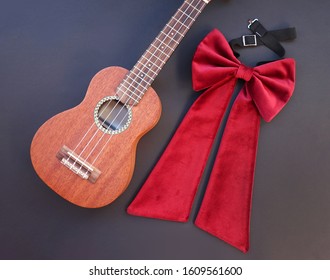 Concept Image Of A Velvet Bow And Ukulele, Top View On Black Background