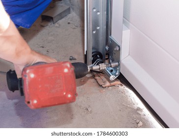 Concept Of Improvement And Building Renovation. Cropped View Of Professional Worker Install Metal Rail On Garage Door System In New House Under Construction, Using Electric Screwdriver