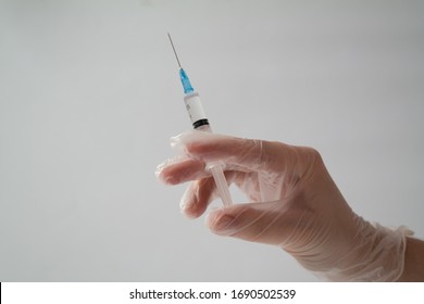 The Concept Of Inoculation, Vaccination Or Treatment Of The Disease. Close-up Of The Doctor's Gloved Hand Holding A Medical Syringe On A Gray Background.