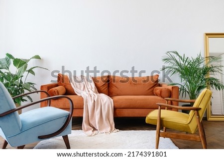 Concept interior design in the style of the 80s. Front view of elegant living room with vintage orange sofa, blue and yellow armchairs. Ergonomic couch in bright apartment with retro interior design