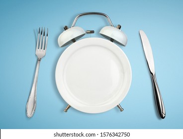 Concept Of Intermittent Fasting, Diet And Weight Loss. Plate As Alarm Clock On Blue