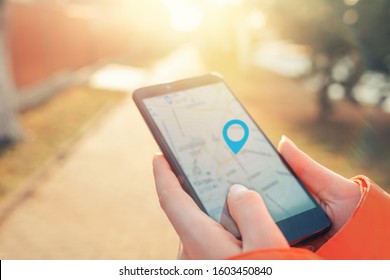 Concept of Internet maps and navigation. Women's hands hold a smartphone with a map application, and a marked icon of the location. Light