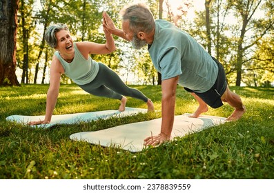 Concept of joint workout. Athletic man and woman standing in plank position with outstretched arms and giving high five to each other. Happy team of husband and wife training together on fresh air. - Powered by Shutterstock