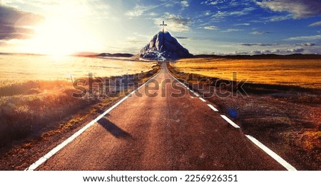Concept of the journey towards destiny and spirituality.Landscape of crop fields and grassy meadows at sunset and road or path to the mountain with cross on top. 