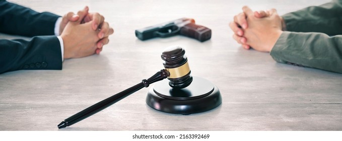 Concept Of Judging, Competition And Fairness In Business, Businessman Hand With Wooden Gavel And Gun On Wooden Table.