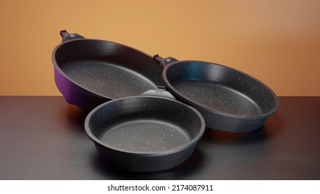 Concept of kitchen utensils, close up of new set of frying pans lying on the table. Action. New modern non stick pans.