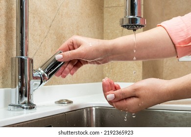 The Concept Of Lack Of Tap Water. The Faucet Has No Running Water. Drops Of Water Drip From Faucet In Human Palm Above Metal Kitchen Sink