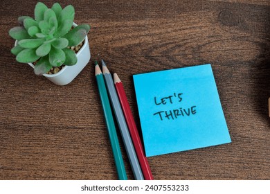 Concept of Let's Thrive write on sticky notes isolated on Wooden Table.