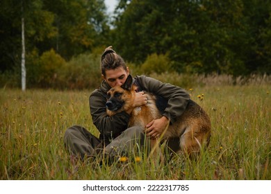 Concept of love and loyalty with animal. Male pet owner sits in grass in autumn and hugs dog. Young Caucasian man with dreadlocks and beard kisses German Shepherd. - Powered by Shutterstock