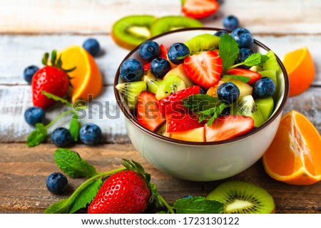Concept of low calories delicious desserts. Summer fresh bowl with colorful fruit salad. Healthy natural organic food. Tasty sweet snack, light simple tasty lunch. Close up macro view wooden backgroun