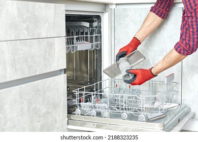 Concept maintenance service of home appliances. Worker cleans filter in the dishwasher. Male repairman checking food residue filters.