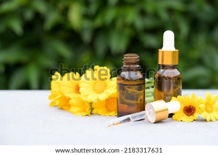 Concept of making natural cosmetics at home - dropper bottles with calendula oil against green leaves as natural background. Herbal cosmetic oil for skincare or essential oil for aromatherapy. Mockup