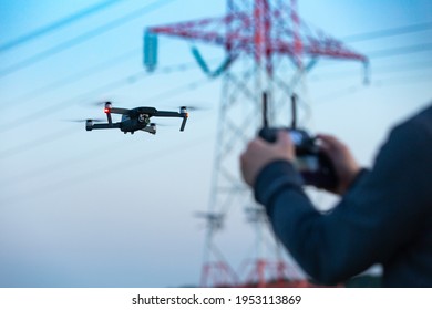A concept of a man flying a drone collecting a data remotely from a power tower station or for telecommunication. Drone safety, power lines.