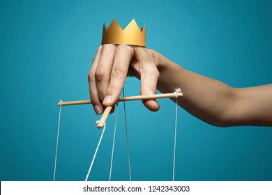 Concept of manipulation. Hand with crown holds strings for manipulation on blue background.
