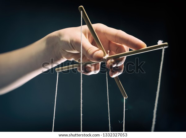 Concept of manipulation. Hand holds strings\
for manipulation. On dark\
background.