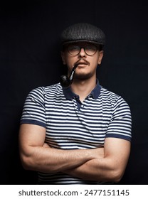 Concept of masculinity with a sailor in a cap and crossed arms. Close-up portrait of a sailor with a cradle cap and muscular arms. Black background.