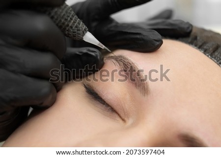 Concept of microblading eyebrows. The cosmetologist performs the procedure of permanent makeup of the eyebrows in close-up.