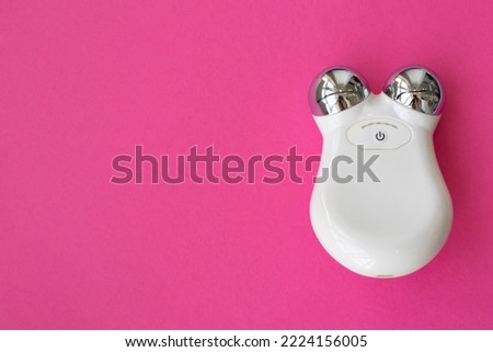The concept of microcurrents. Microcurrent Facial Massager. Device for home use to fight aging and tighten the face on a pink background. Top view, flat plan, space for text