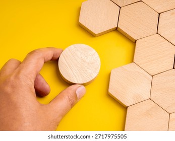 Concept of mismatch and problem solving with hand holding a round wooden piece not fitting into hexagon space. Symbolizes difference, challenge, creativity, unique thinking, and solution development.