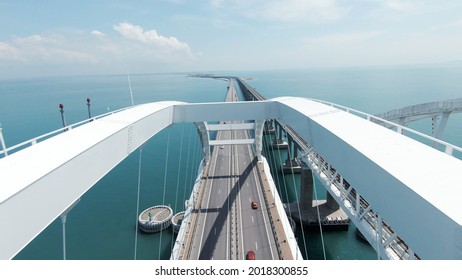 Concept of modern architecture, long white beautiful bridge above the endless sea. Shot. Cars driving the wide new bridge on cloudy sky background.