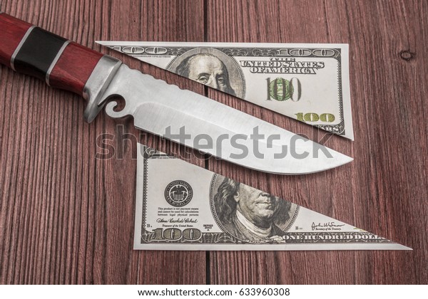 Concept of money share, cutting money\
banknotes 100 dollars with a knife Two half objects lie on a wooden\
kitchen board. Natural material. Business,\
crime.