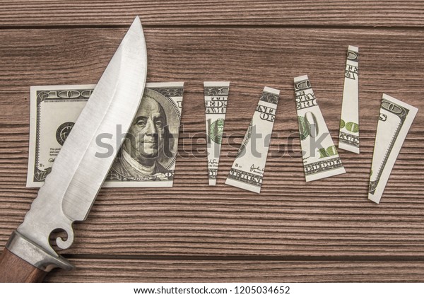 The concept of money is to\
share, cutting money notes 100 dollars with a knife. A cut banknote\
lies on a wooden kitchen board. Natural material. Business,\
crime.